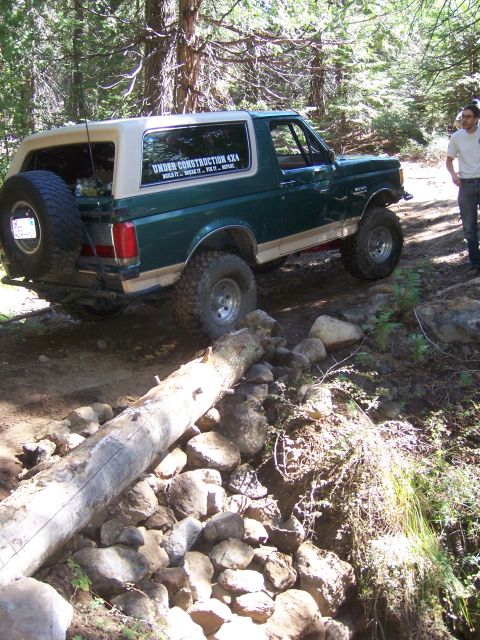 1991 Ford Bronco - A green Ford Bronco navigates a challenging off-road trail, with a fallen log blocking the path.