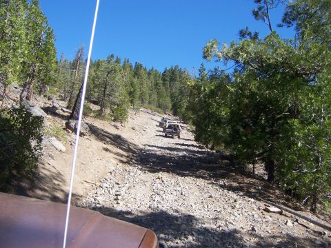 1991 Ford Bronco - Multiple SUVs navigate a challenging, rocky off-road trail under a clear blue sky.