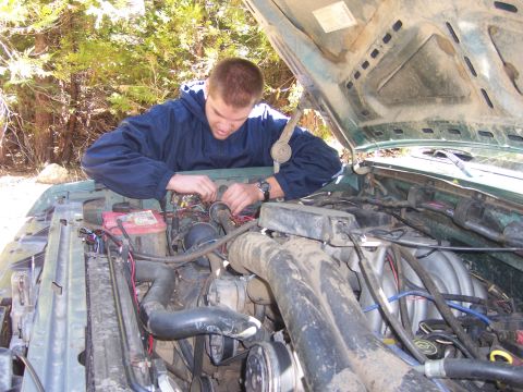 1991 Ford Bronco - A person is seen working on the engine of a green vehicle with the hood open.