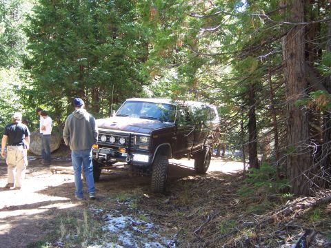 1991 Ford Bronco - Ford Bronco navigating a wooded trail with snow patches on the ground.