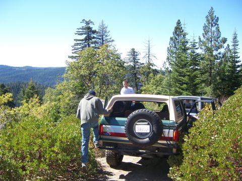 1991 Ford Bronco - 1991 Ford Bronco on a dirt road, with a spare tire on the back and two people around it.