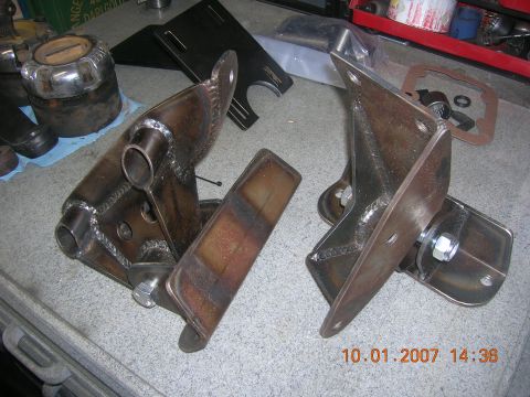 1996 Ford Bronco - Close-up of custom-fabricated metal brackets, likely for automotive use, on a workshop surface.