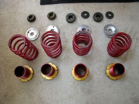 1994 Ford Probe - Various automotive suspension components, including red coil springs and metal perches, are arranged on a carpeted surface.
