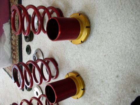 1994 Ford Probe - Several red coilover suspension assemblies and associated parts are displayed on a carpeted floor.