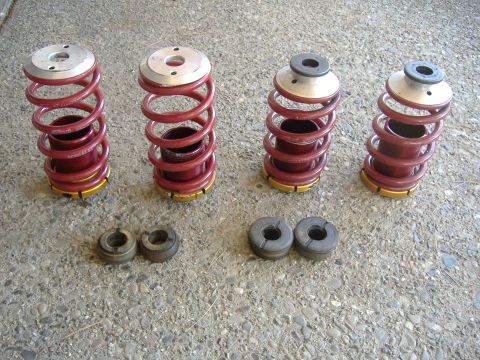 1994 Ford Probe - Four suspension coilover assemblies and four rubber isolators are laid out on a concrete surface.
