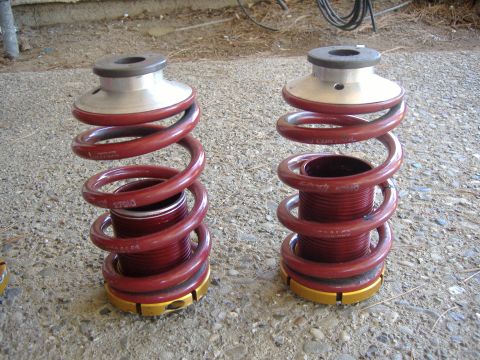 1994 Ford Probe - Pair of red coilover suspension springs with adjustable collars sit on a gravelly surface.