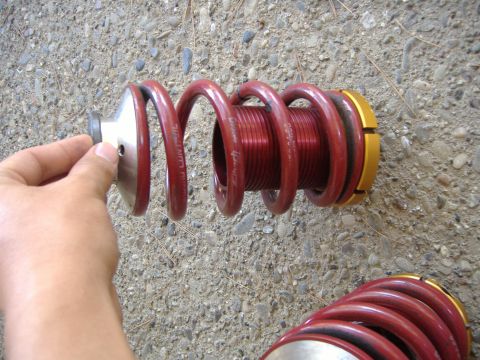 1994 Ford Probe - A red coilover suspension part is held by a hand against a gravelly surface.