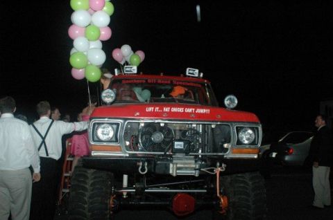 1979 Ford Bronco - A lifted red truck, possibly a 1979 Ford Bronco, decorated with balloons and a funny quote, stands ready for an event.