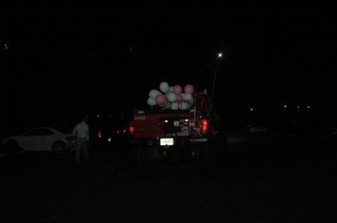 1979 Ford Bronco - A red pickup truck is seen at night with a load of balloons in its bed, next to a white car.