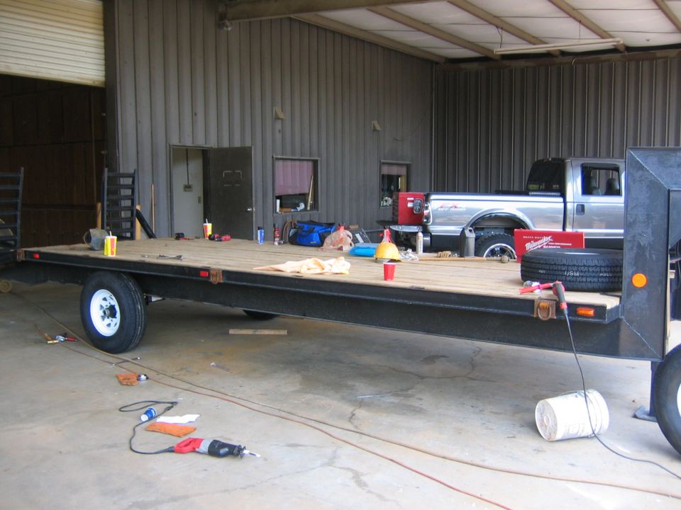 Flatbed trailer in front of a silver pickup truck inside a garage. Tools and supplies are on the trailer