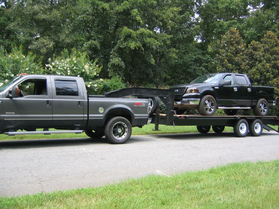 Black Ford F-150 on trailer, towed by grey Ford F-250