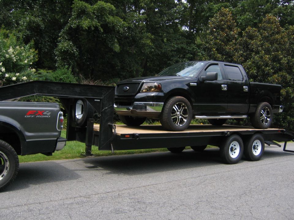Black Ford F-150 pickup truck loaded on a dual-axle flatbed trailer, being towed by another truck