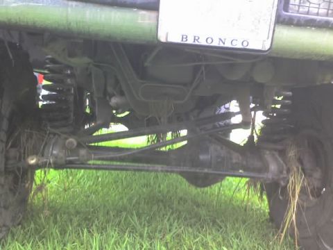 1995 Ford Bronco - The underside of a green Ford Bronco is visible, with suspension and drivetrain components obscured by grass and mud.