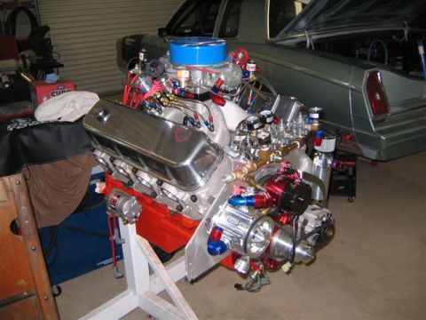 1995 Ford Bronco - A highly modified V8 engine is displayed on a stand, with a car in the background.