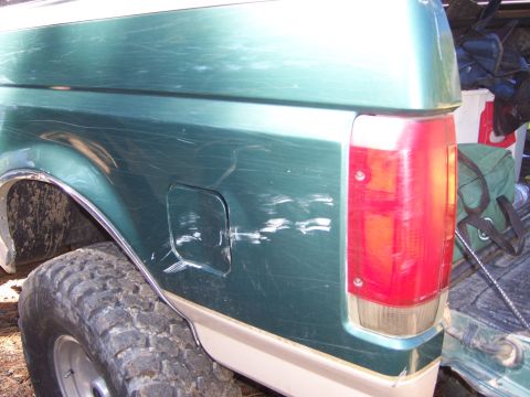 1991 Ford Bronco - Scratched green and tan pickup truck rear with a visible fuel door and taillight.