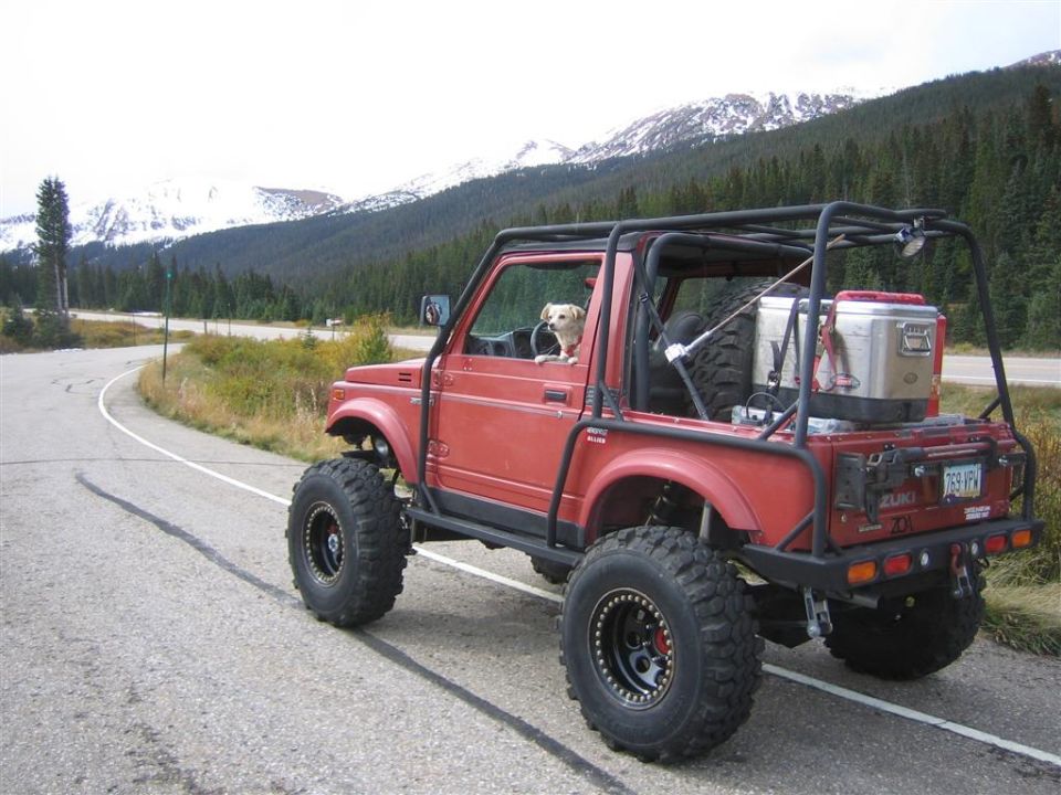 Lifted red Suzuki Samurai with exo cage and dog in window on a mountain roadside