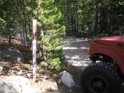 1987 Suzuki Samurai - A red off-road vehicle is parked next to a trail marker in a wooded area.