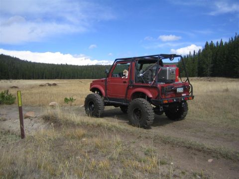 1987 Suzuki Samurai - Modified 1987 Suzuki Samurai on a dirt trail with a forest in the background.