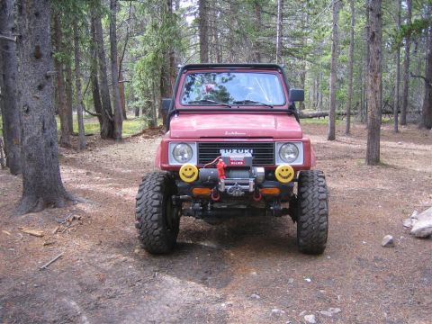 1987 Suzuki Samurai - This 1987 Suzuki Samurai is equipped with a winch and custom smiley face lights, parked in a wooded area.