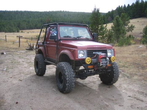 1987 Suzuki Samurai - Modified 1987 Suzuki Samurai off-roader on a dirt path with trees in the background.