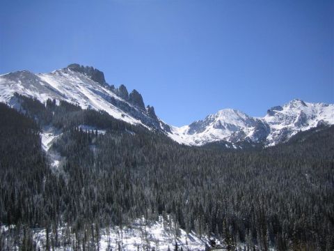 1999 Ford F-250 - A vast mountain landscape with snow-capped peaks and a thick forest below, under a bright blue sky.