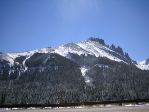 1999 Ford F-250 - A mountain range covered in snow and surrounded by dense evergreen trees under a clear blue sky.