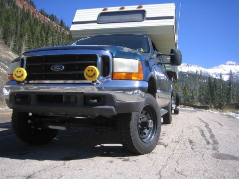 1999 Ford F-250 - A 1999 Ford F-250 Super Duty pickup truck is equipped with a camper and parked on a scenic mountain road.
