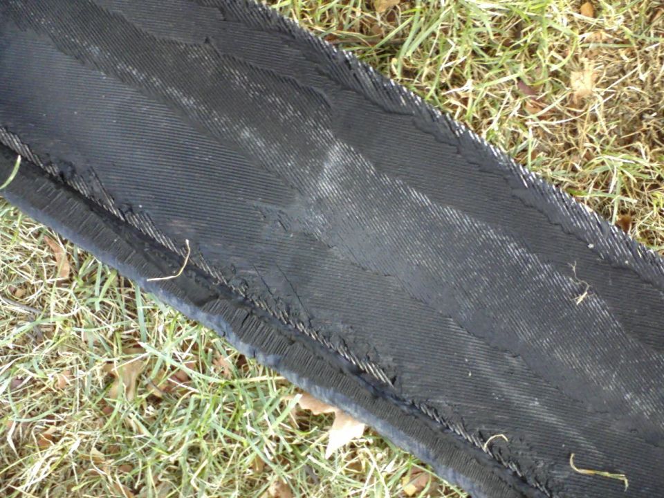 Black shredded rubber belt or tire piece with frayed edges on grass