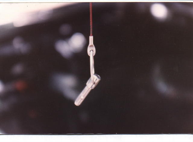 Close-up of a small metal hook pin hanging from a thin cable against a dark blurred background