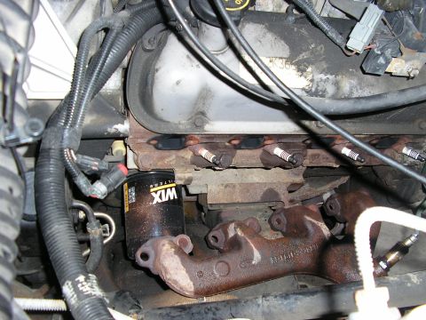 1996 Ford Bronco - Close-up down the passenger side of a V8 engine bay with the exhaust manifold removed and resting on the frame rail, showing the bare cylin…