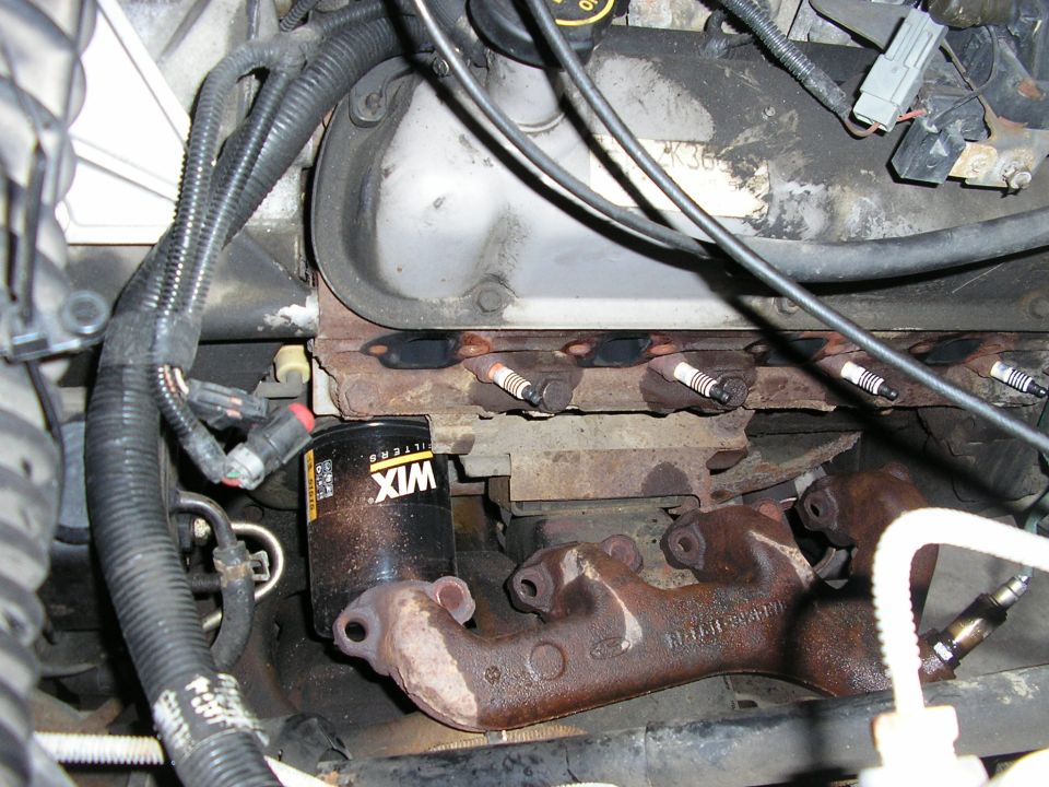 V8 cylinder head with spark plugs exposed and rusty exhaust manifold removed, WIX oil filter nearby