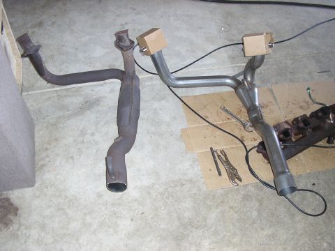 1996 Ford Bronco - Side-by-side comparison on a garage floor of a rusty stock exhaust Y-pipe with its bulged factory section next to a new mandrel-bent stainl…