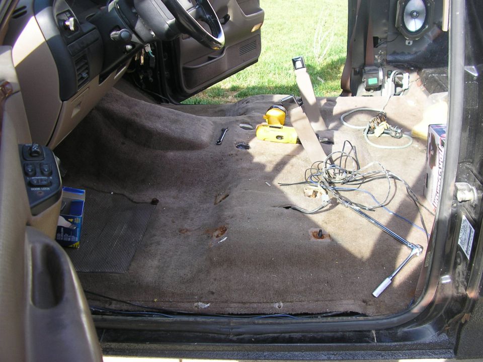 Ford truck interior with front seats removed, brown carpet, tools and wiring on the floor