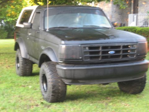 1995 Ford Bronco - A black Ford Bronco with a white top and lifted suspension sits on a grassy lawn.