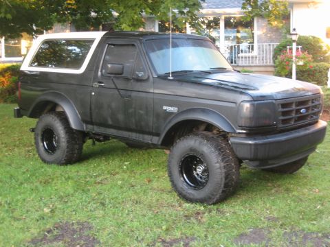 1995 Ford Bronco - Black 1995 Ford Bronco with white removable top parked on grass in front of a house.