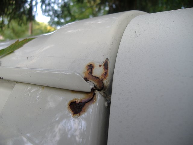 Close-up of rust on a white vehicle's body panel, showing peeling paint