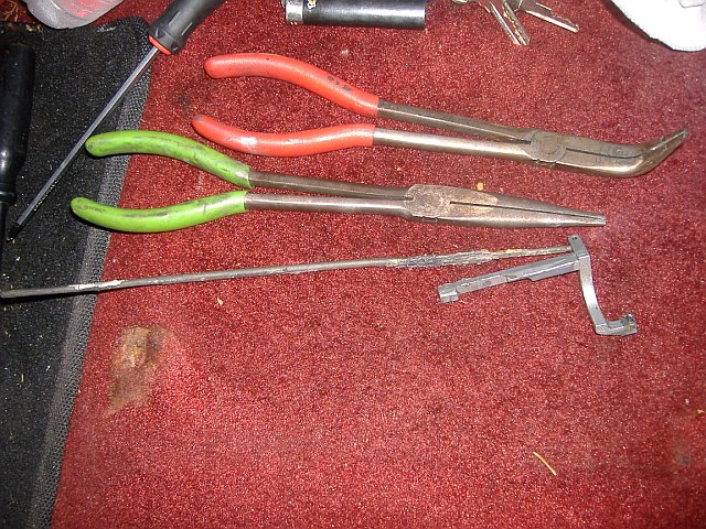 Several long-nosed pliers and a screwdriver on red carpet. A metal clip is also visible