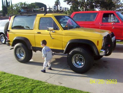1996 Ford Bronco - A yellow Ford Bronco is parked next to a red Ford Bronco, with a child standing nearby.
