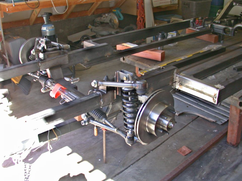 Bare chassis frame on sawhorses with front coilover suspension, disc brakes, and rack-and-pinion steering installed