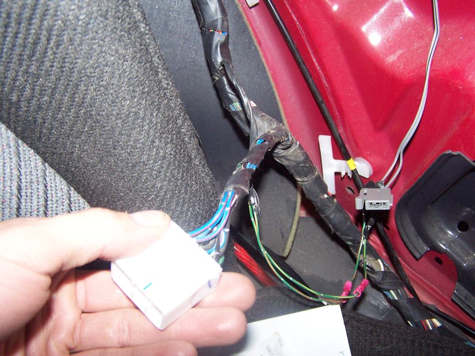 Hand holding a white wiring harness connector with blue and green wires; other wires are taped and connected with red crimp connectors