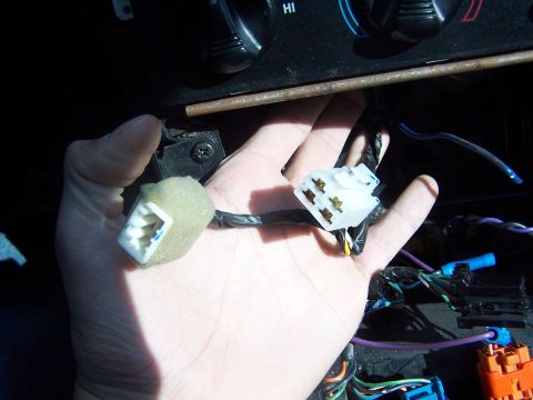 1994 Ford Probe - Close-up of a hand holding electrical connectors within a vehicle's dashboard area, with part of the climate control visible.