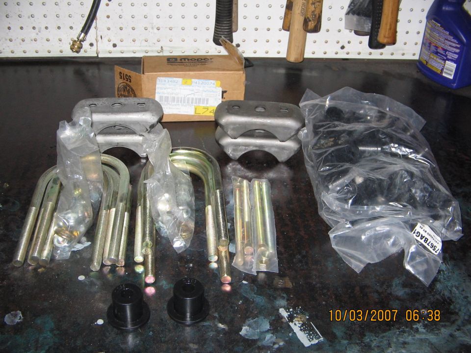 Leaf spring U-bolts, spring plates, bushings and hardware laid out on a workbench with a Mopar parts box