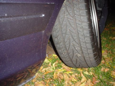 2000 Ford Crown Victoria - A flat tire is visible on the side of a purple vehicle parked on grass with fallen leaves.