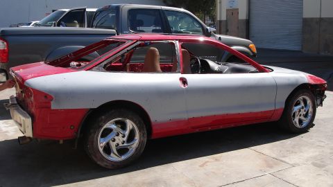 1996 Ford Probe - This red and gray car, possibly a Ford Probe, is seen from the side with its windows and doors removed, indicating it is in a state of repa…