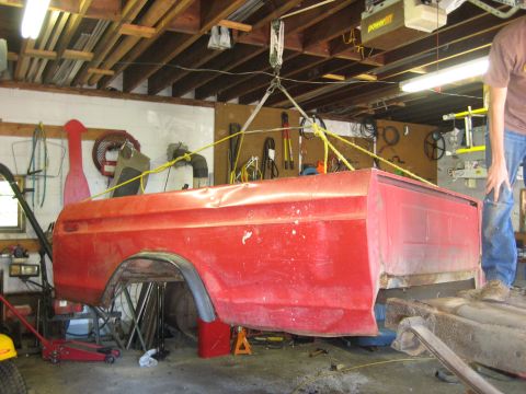 1990 Ford Bronco - Red pickup truck bed hoisted in garage, likely for repair or replacement.
