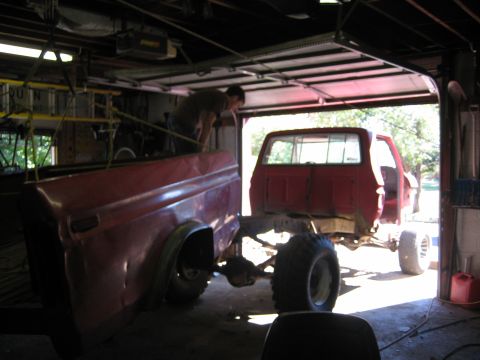 1990 Ford Bronco - Red pickup truck bed and chassis in garage, with a person working on it.