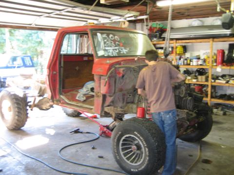 1990 Ford Bronco - A person works on the engine of a red pickup truck inside a garage, with another vehicle in the background.