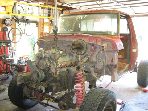 1990 Ford Bronco - This red truck chassis, likely from the 1970s, is undergoing repairs in a garage.