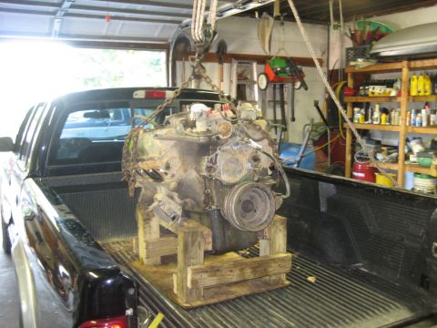 1990 Ford Bronco - Engine being loaded into a truck bed in a garage setting.