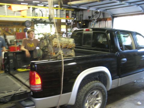 1990 Ford Bronco - An engine is loaded into the bed of a black pickup truck inside a garage.
